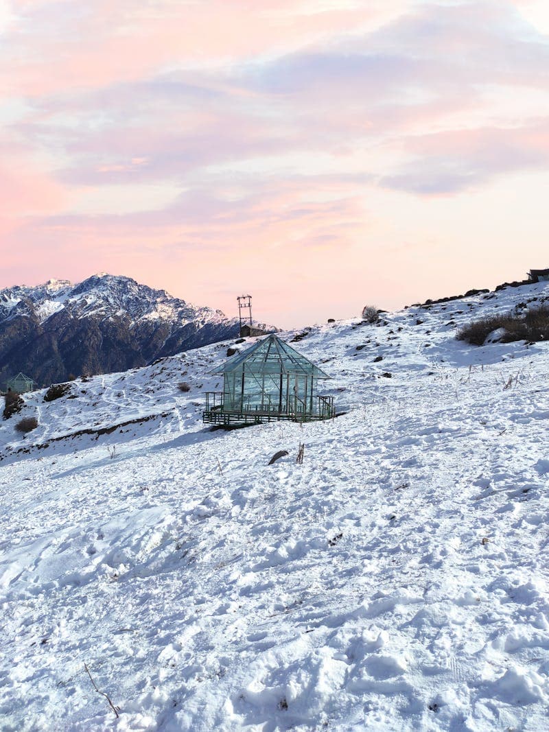 A glass greenhouse structure standing in a snowy winter landscape at sunset
